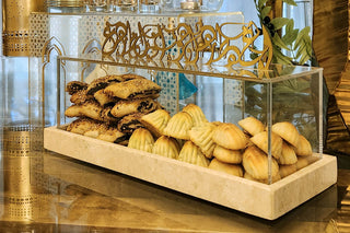 Image Alhambra Dessert Box Clear acrylic dessert box on Travertine marble tray and gold Metal Calligraphy Dinning Table showing pastry items