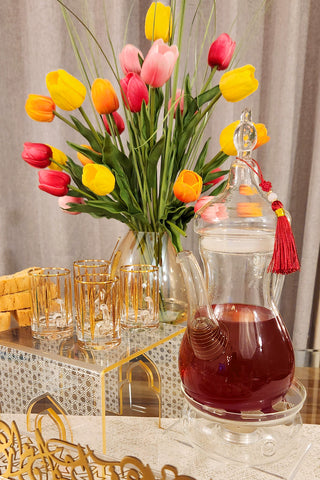 Image Ibreeq a turkish style teapot with tea inside next to Anater food riser and tea cups and flower background.